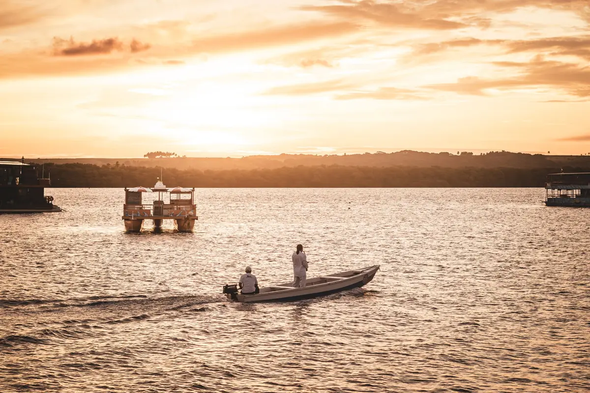 Dois pescadores num barco pequeno em águas douradas no fim da tarde