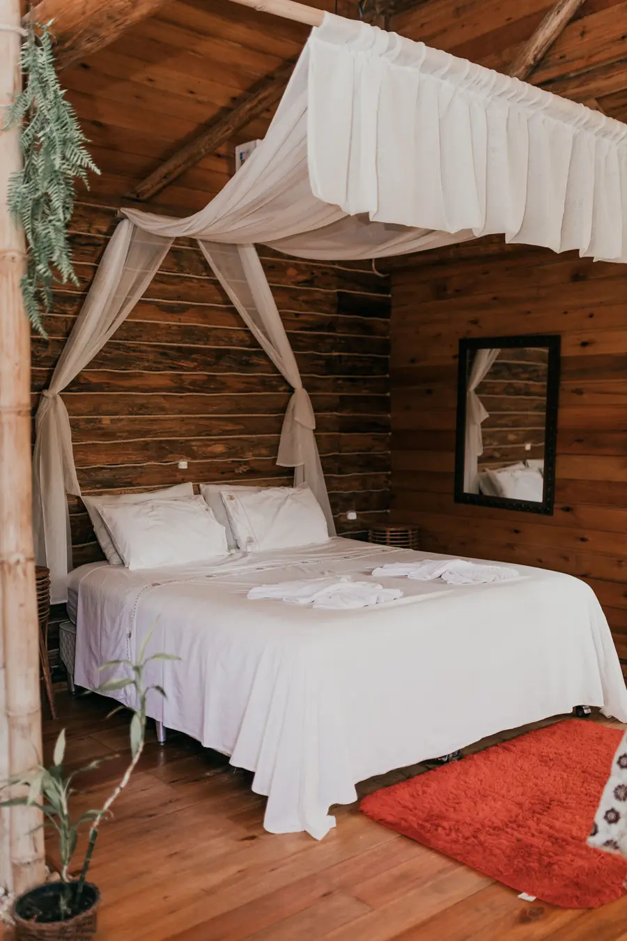 Quarto com paredes de madeira e cama de casal com dossel de tecido branco