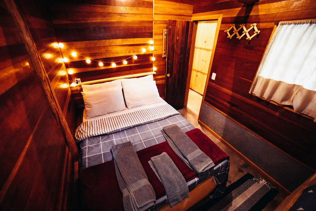 Cama de casal com manta xadrez num quarto de madeira iluminado por luzinhas